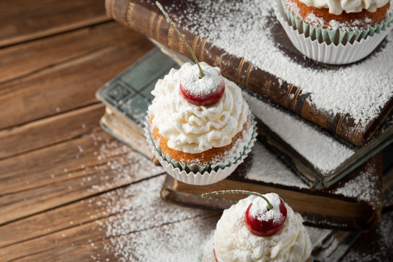 closeup-shot-delicious-cupcakes-with-cream-powdered-sugar-cherry-top-books.jpg